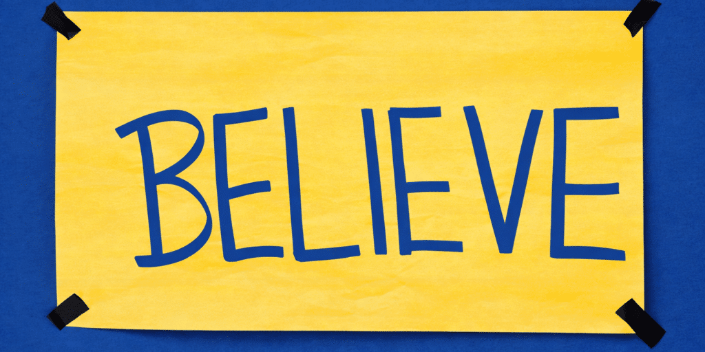 A yellow paper with the word "BELIEVE" in large blue letters, taped to a blue background at the corners with black tape, inspires an abundance mindset.